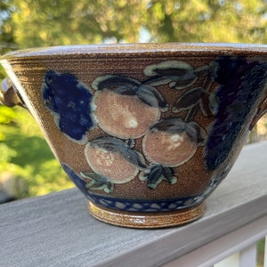 May include: A brown ceramic bowl with two handles. The bowl is decorated with a blue and white floral design and has a brown glaze.