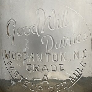May include: A vintage glass milk bottle with a white label that reads "Good Will Dairies, Morganton, N.C. Grade A Pasteurized Milk".