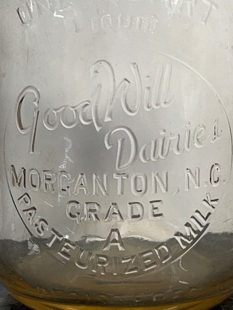 May include: A vintage glass milk bottle with a white label that reads "Good Will Dairies, Morganton, N.C. Grade A Pasteurized Milk".