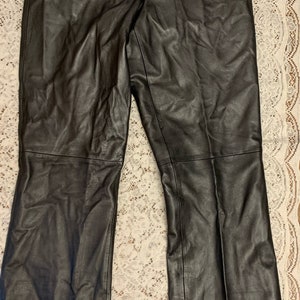 May include: Black leather pants with a braided waistband and a slight flare at the bottom.