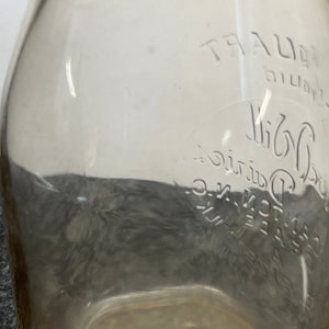 May include: A clear glass milk bottle with the text "TRAUER Dairy Co. Inc. - Elgin, Ill." embossed on the side.