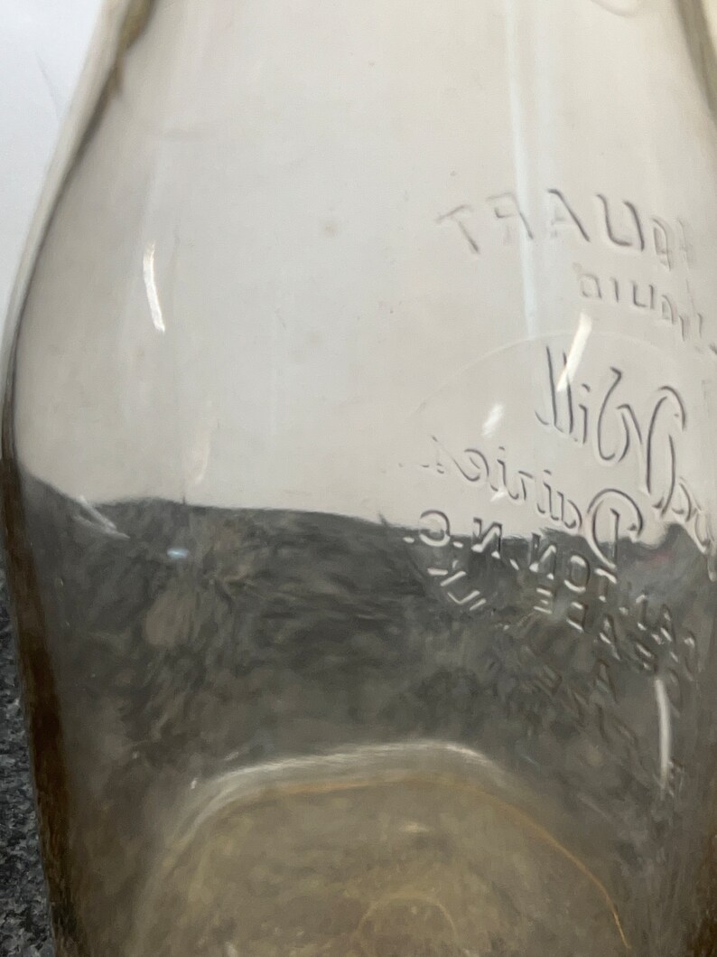 May include: A clear glass milk bottle with the text "TRAUER Dairy Co. Inc. - Elgin, Ill." embossed on the side.