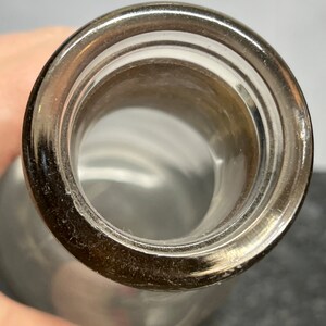 May include: Close-up of the top opening of a clear glass bottle with a smooth, rounded lip.