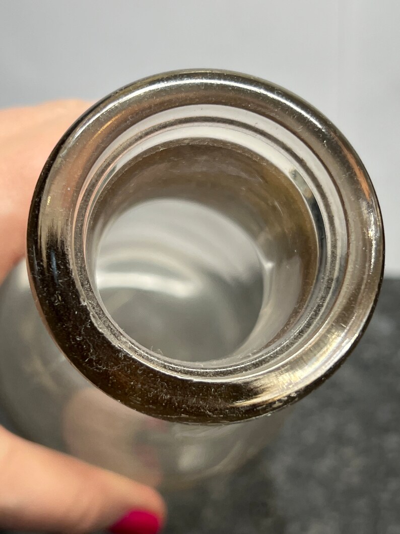 May include: Close-up of the top opening of a clear glass bottle with a smooth, rounded lip.