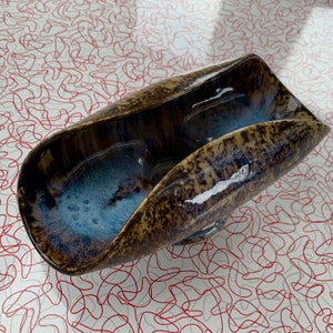 May include: A brown and blue ceramic serving dish with a unique, wavy design. The dish has a glossy finish and is perfect for serving snacks or appetizers.