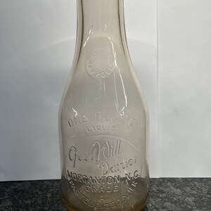 May include: A clear glass milk bottle with the words "Good Will Dairies" and "Morgantown, N.C." etched into the side. The bottle is labeled "Past. Grade A" and "Pasteurized Milk".