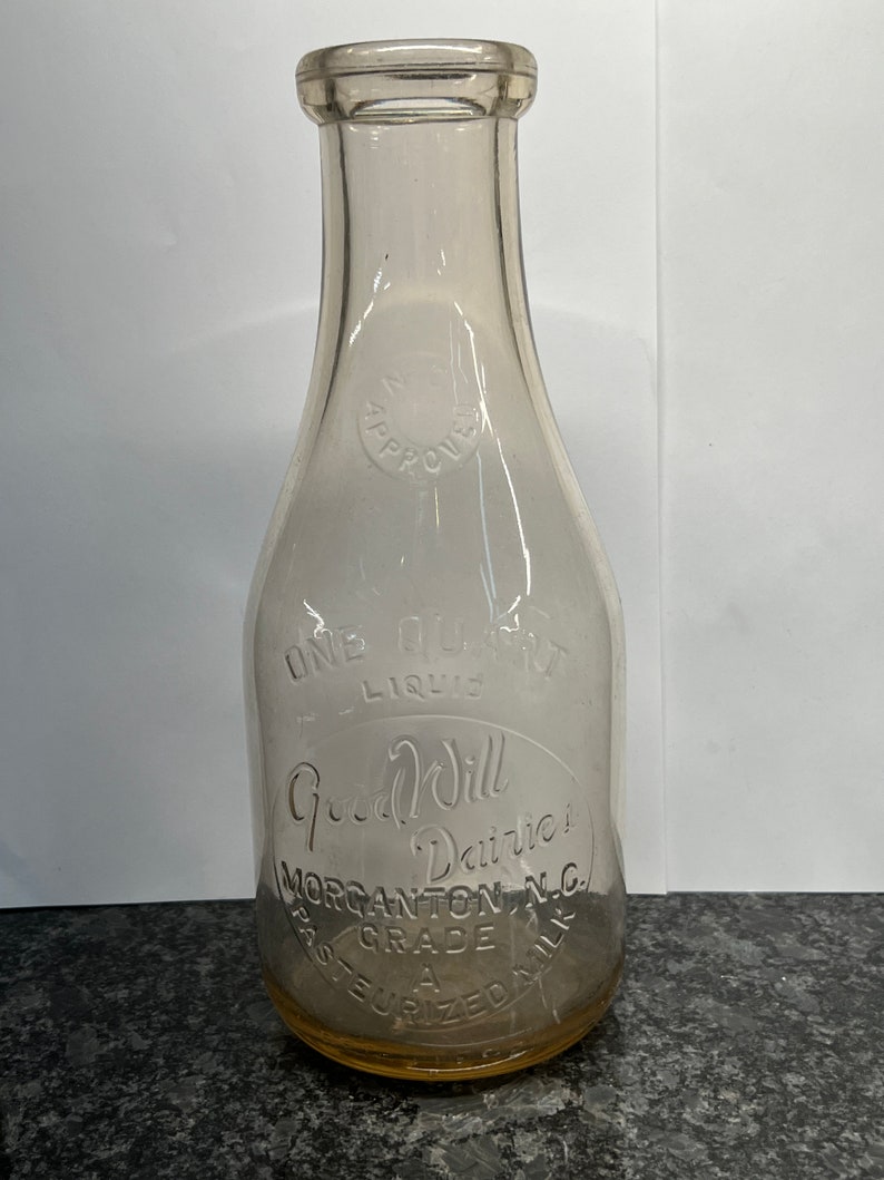 May include: A clear glass milk bottle with the words "Good Will Dairies" and "Morgantown, N.C." etched into the side. The bottle is labeled "Past. Grade A" and "Pasteurized Milk".