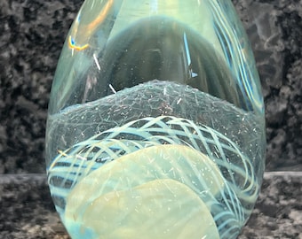Könnte beinhalten: Ein durchsichtiger Glas-Briefbeschwerer mit einem weißen Wirbelmuster im Inneren. Der Briefbeschwerer hat die Form eines Eies.
