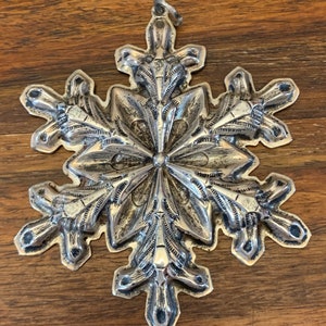 May include: A silver snowflake ornament with intricate details. The snowflake is made of metal and has a loop at the top for hanging.