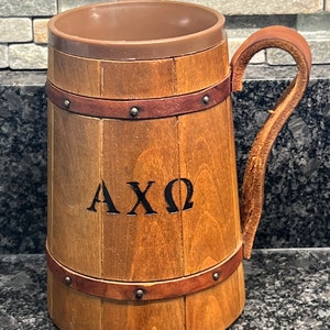 May include: A wooden beer stein with a brown leather handle and the letters "AXO" carved into the side.