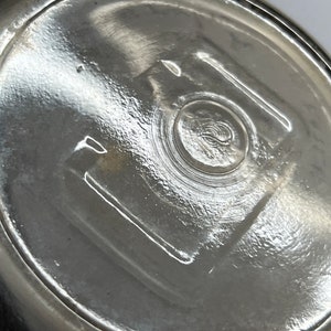 May include: Close-up of the bottom of a clear glass jar with a textured surface and a circular indentation in the center.