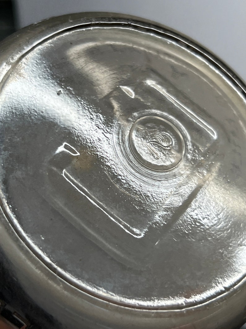 May include: Close-up of the bottom of a clear glass jar with a textured surface and a circular indentation in the center.