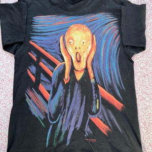 May include: Black t-shirt with a colorful print of Edvard Munch's "The Scream". The print features a person with a distorted face screaming, with a wavy background and a red bridge.
