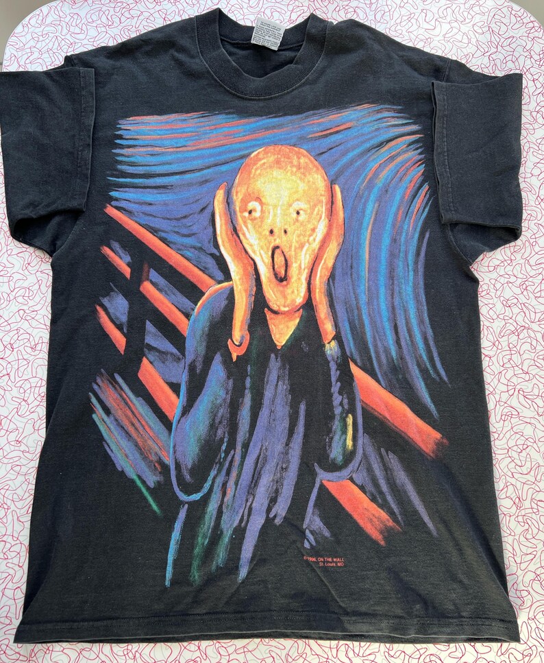 May include: Black t-shirt with a colorful print of Edvard Munch's "The Scream". The print features a person with a distorted face screaming, with a wavy background and a red bridge.