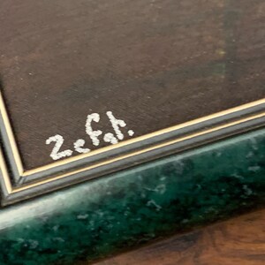 Puede incluir: Primer plano de un marco verde con un borde dorado. La firma "Z. Fah." est&aacute; escrita en pintura blanca sobre la superficie marr&oacute;n del marco.