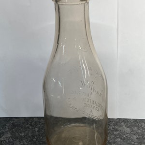 May include: A clear glass milk bottle with a textured surface. The bottle has the text "REFRIGERATED MILK GRADE A DECANTON CO. JERSEY DAIRY" embossed on the side.