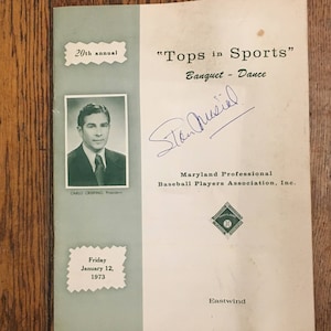 May include: A black and white photo of a man in a suit and tie. The photo is on a white paper with the text "20th annual" and "Tops in Sports" in black text. The text "Banquet - Dance" is also in black text. The man's name is "Stan Musial" and is written in blue ink. The text "Maryland Professional Baseball Players Association, Inc." is in black text. The text "Friday January 12, 1973" is in black text. The text "Eastwind" is in black text.