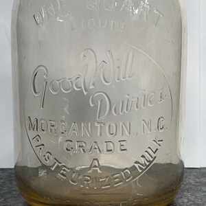 May include: A clear glass milk bottle with a yellow rim. The bottle has the text "Good Will Dairies" and "Morgantown, N.C. Grade A Pasteurized Milk" embossed on the side.
