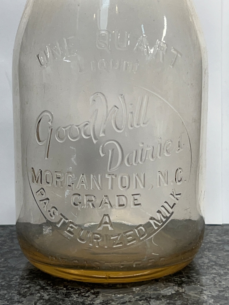 May include: A clear glass milk bottle with a yellow rim. The bottle has the text "Good Will Dairies" and "Morgantown, N.C. Grade A Pasteurized Milk" embossed on the side.