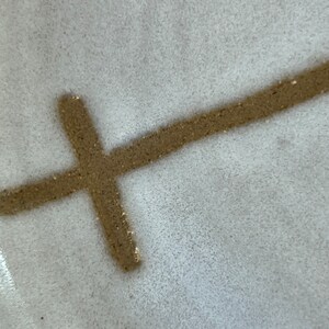 May include: A close-up of a white ceramic plate with a brown cross drawn on it.