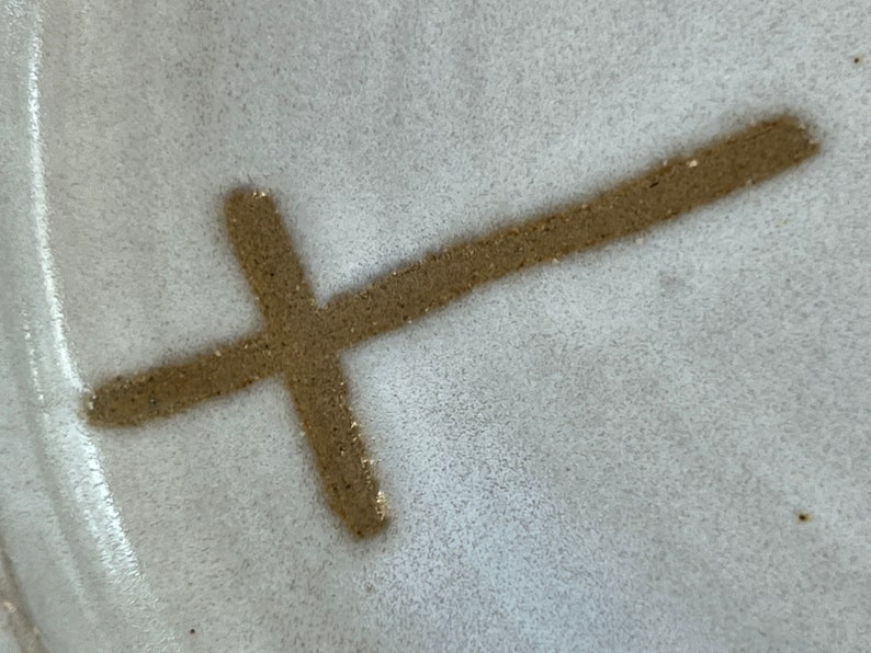 May include: A close-up of a white ceramic plate with a brown cross drawn on it.