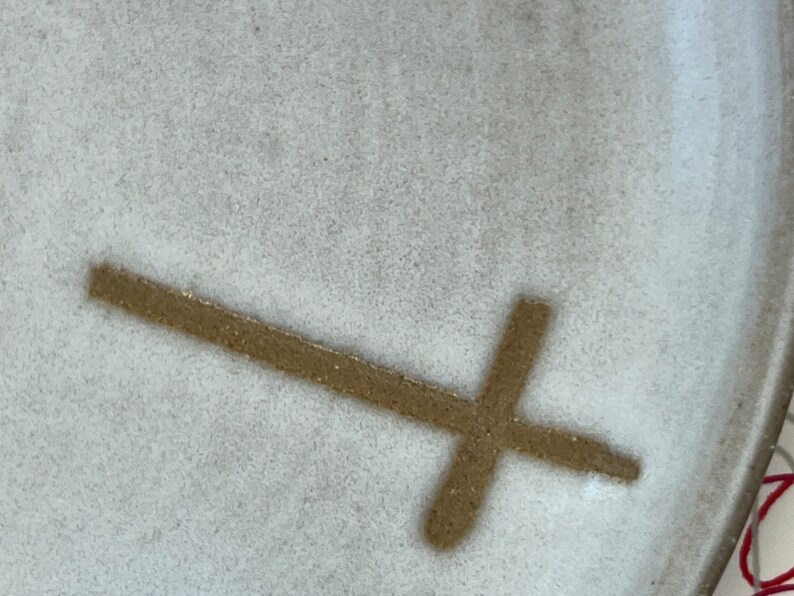 May include: A white ceramic plate with a brown cross design.