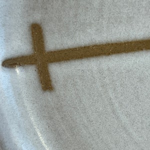 May include: A close-up of a white ceramic plate with a brown cross design.
