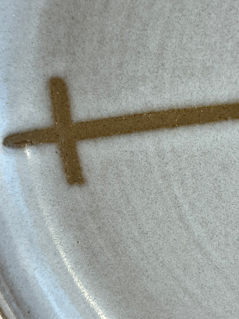 May include: A close-up of a white ceramic plate with a brown cross design.