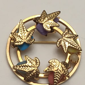 May include: Gold tone brooch with a circular design featuring five stylized leaves with colorful stones in the center of each leaf.