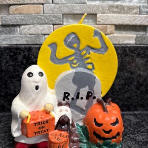May include: A Halloween-themed figurine set featuring a ghost holding a "Trick or Treat" bag, a pumpkin, a tombstone with "R.I.P.", and a skeleton against a yellow moon. The figurines are painted in orange, white, gray, and green.