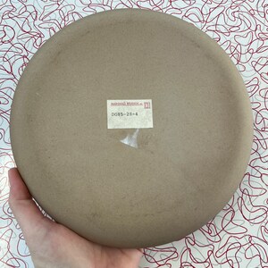 May include: A brown ceramic plate with a white label that reads "MARSHALL STUDIOS INC. DG85-28-4".