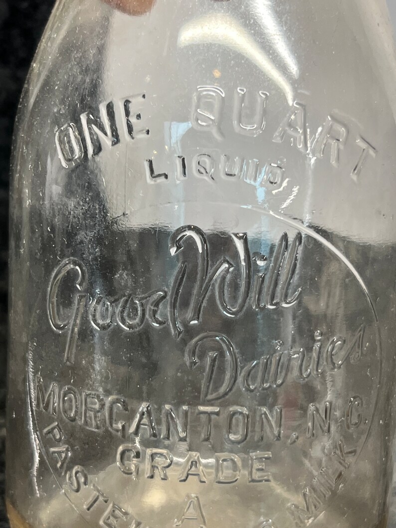 May include: A clear glass milk bottle with the text "One Quart Liquid Good Will Dairies Morgantown, NC Pasteurized Grade A Milk" embossed on the side.