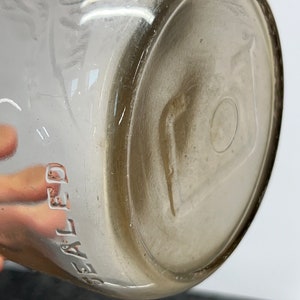 May include: Close-up of the bottom of a clear glass bottle with the word "SEALED" embossed on the side.