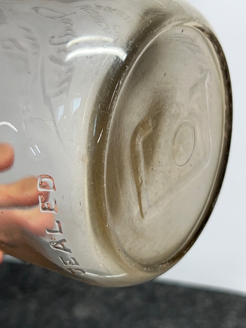 May include: Close-up of the bottom of a clear glass bottle with the word "SEALED" embossed on the side.