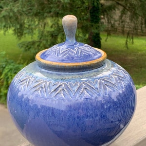 May include: A blue ceramic jar with a lid and a decorative chevron pattern. The jar has a glossy finish and a rounded shape.