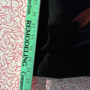 May include: A close-up of a black fabric with a green measuring tape. The tape reads "Remodeling Company" and has markings in inches from 15 to 22.