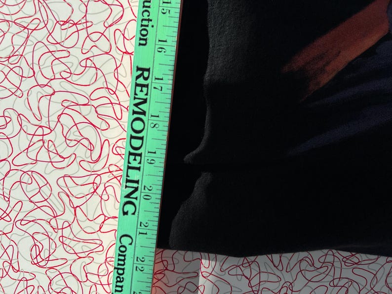 May include: A close-up of a black fabric with a green measuring tape. The tape reads "Remodeling Company" and has markings in inches from 15 to 22.
