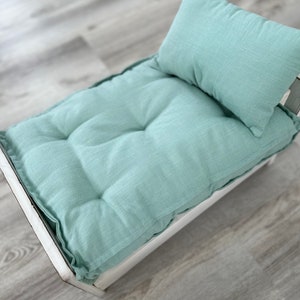 May include: A light green padded bed with a matching pillow. The bed is made of wood and has a white finish.