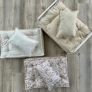 May include: Three white and cream-colored cushions with floral patterns. The cushions are filled with a soft, fluffy material and have a tufted design. The cushions are perfect for adding a touch of comfort and style to any room.