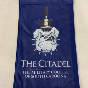 May include: A blue flag with a white bulldog wearing a black and gold hat. The text "THE CITADEL THE MILITARY COLLEGE OF SOUTH CAROLINA" is printed on the flag.