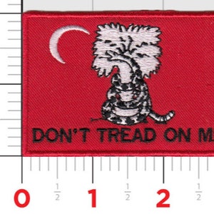 May include: A red embroidered patch with a white rattlesnake coiled around a tree and the words "DON'T TREAD ON ME".