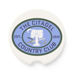 May include: White ceramic coaster with a blue and green oval design. The oval features the text "The Citadel Country Club" with the text "Est. 1842" and a white palmetto tree with crossed swords and a golf club.
