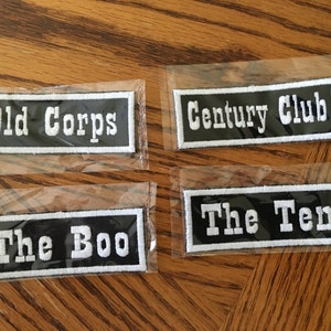 May include: Four black and white embroidered patches with white text on a black background. The patches read "Old Corps", "Century Club", "The Boo", and "The Ten".