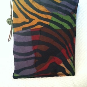 May include: A patchwork zippered pouch with a zebra print design in shades of brown, black, purple, green, and red. The pouch has a brown leather zipper pull with a small round brown button.