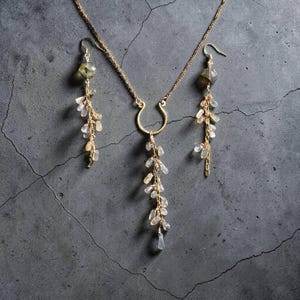 May include: A gold-toned necklace and matching earring set featuring delicate chains adorned with small, translucent, teardrop-shaped stones. The necklace includes a central horseshoe-shaped element with a cascading cluster of stones.