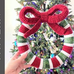 May include: A red, white and green crocheted Christmas wreath with a large red bow. The wreath is hanging on a Christmas tree.