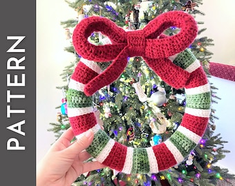 May include: A red, white, and green crocheted Christmas wreath with a large red bow. The wreath is hanging on a Christmas tree.