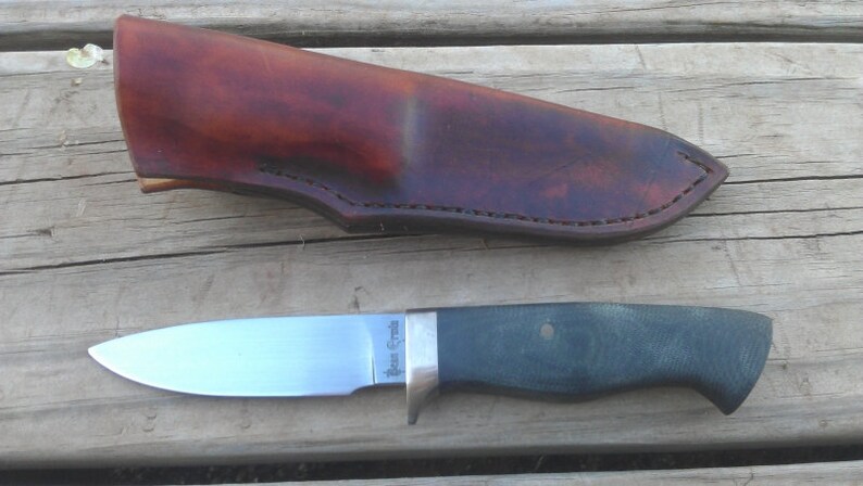 May include: A small, stainless steel knife with a dark green handle and a leather sheath. The knife has the words "Bear Creek" engraved on the blade.