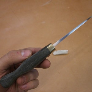 May include: A close-up of a dark green handled knife with a long, thin, silver blade. The knife is held in a hand.