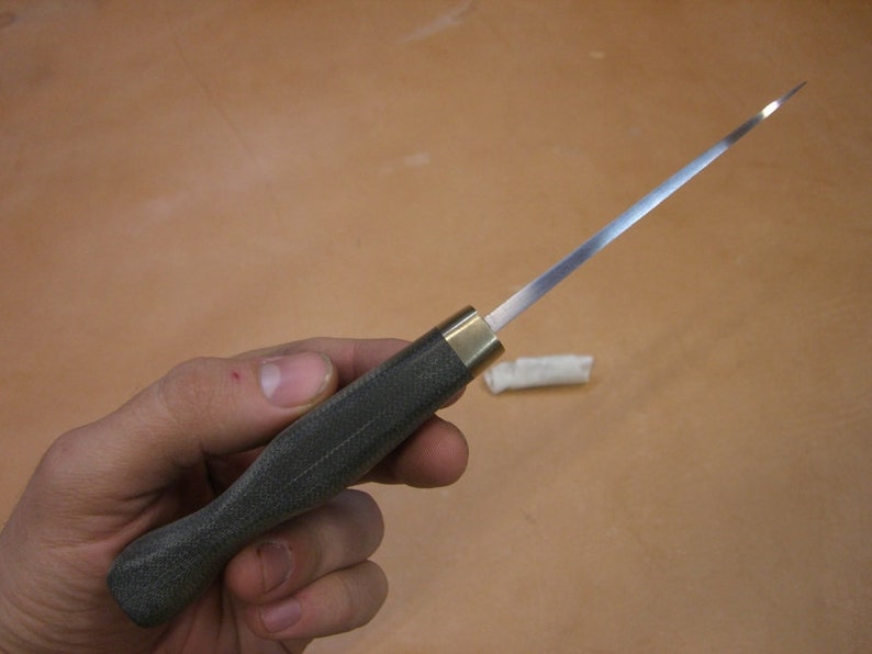 May include: A close-up of a dark green handled knife with a long, thin, silver blade. The knife is held in a hand.